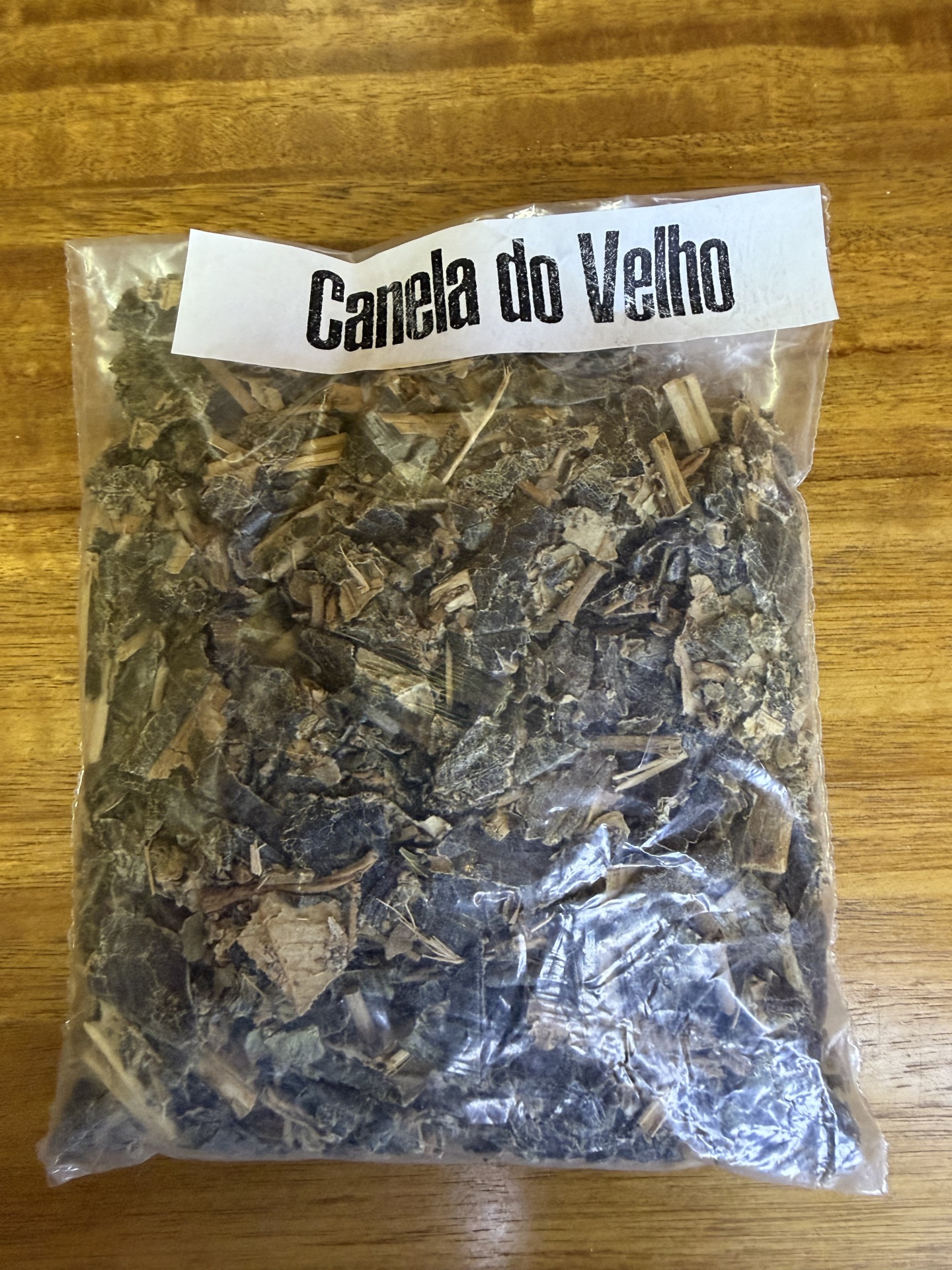 Pacote com planta seca rotulado como Canela do Velho sobre madeira