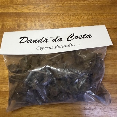 Embalagem plástica com pó escuro e etiqueta Dandá da Costa Cyperus Rotundus sobre mesa de madeira