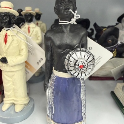 Estátua decorativa de figura humana com saia azul e objeto prateado