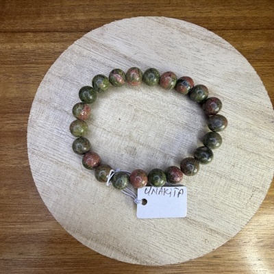 Pulseira de pedra verde e rosa com etiqueta UNAKITA numa superfície de madeira.