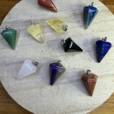 Dez pendentes de pedra polida coloridos com argolas metálicas, dispostos sobre superfície redonda clara