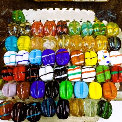 Botões grandes coloridos de vidro com vários padrões e cores, organizados em filas sobre uma superfície rústica.