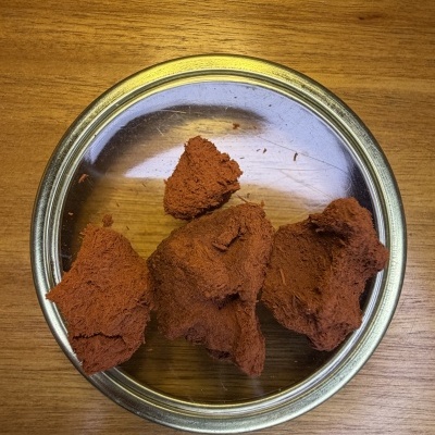 Tigela metálica com pedaços de material marrom avermelhado sobre mesa de madeira