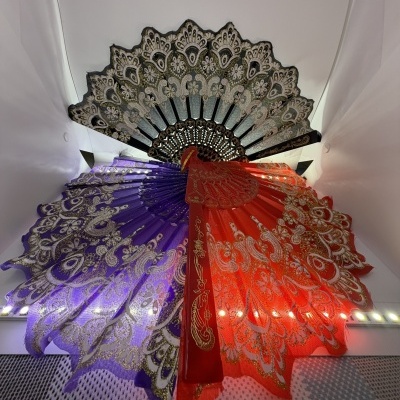 Três leques decorativos coloridos com padrões dourados e pretos numa parede branca
