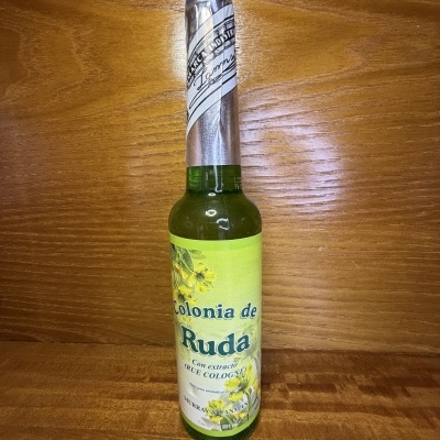 Garrafa verde com rótulo amarelo com flores e texto em cima de superfície de madeira.