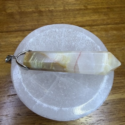 Pingente em pedra multifacetada com suporte metálico sobre base branca circular.