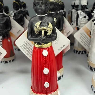 Estatueta de figura com coroa dourada e vestido vermelho com botões brancos.