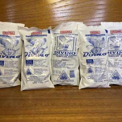 Embalagens brancas do produto Divino para defumar com imagem de pomba e texto em português sobre mesa de madeira.