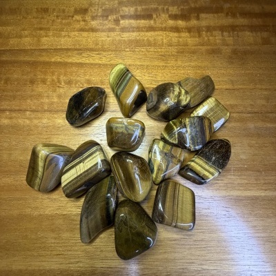Pedras semipreciosas polidas em tons castanho e dourado sobre madeira clara