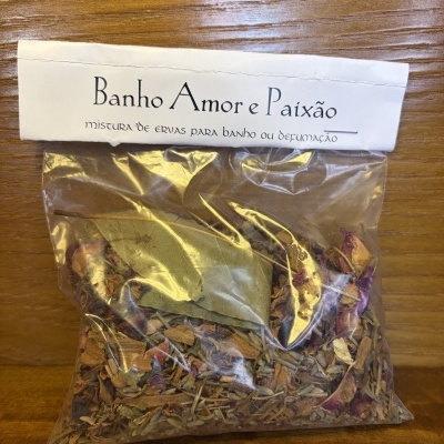 Pacote de ervas secas com etiqueta Banho Amor e Paixão em superfície de madeira.
