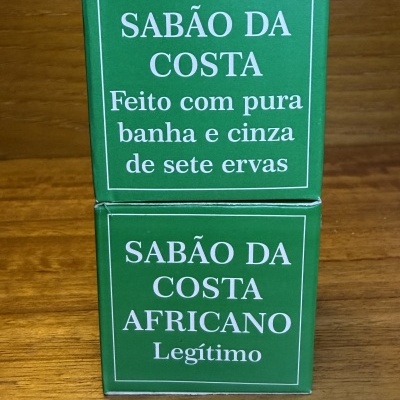 Caixas verdes de sabão Sabão da Costa com texto em português sobre uma superfície de madeira.