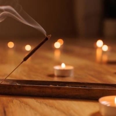 Incenso aceso num suporte de madeira com velas ao fundo