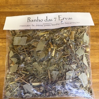 Pacote de ervas secas com etiqueta branca Banho das 7 Ervas sobre mesa de madeira