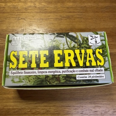 Caixa de incenso Sete Ervas com texto e plantas sobre mesa de madeira