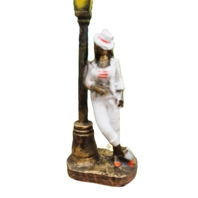 Escultura pequena de figura feminina em roupa branca junto a candeeiro antigo