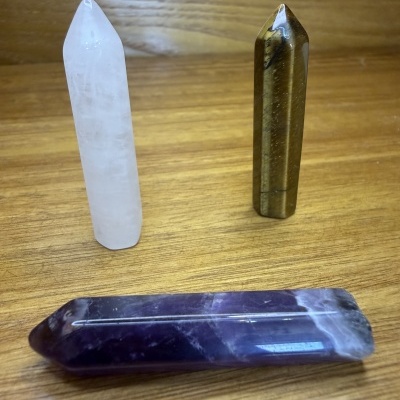 Três lápis de cristal polidos sobre madeira clara, cores branco, castanho e roxo.