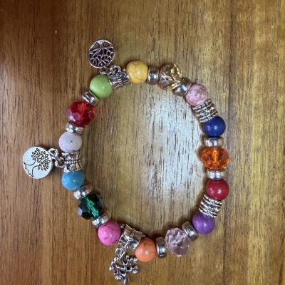 Pulseira colorida com contas e pendentes prateados em fundo de madeira.