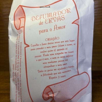 Pacote de papel branco com texto impresso em vermelho e título DEFUMADOR de ERVAS para o Amor.