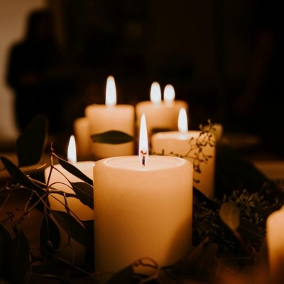 Velas brancas acesas com folhas verdes em ambiente escuro