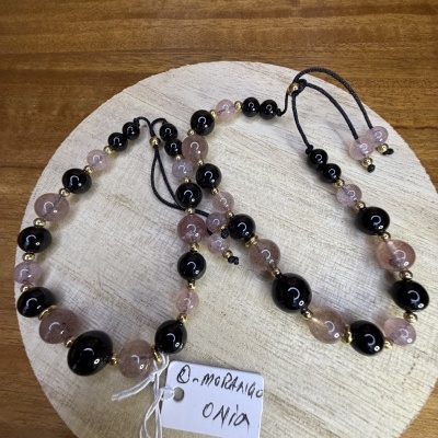 Colar e pulseira com contas cor-de-rosa translúcido, preto e dourado sobre base de madeira clara