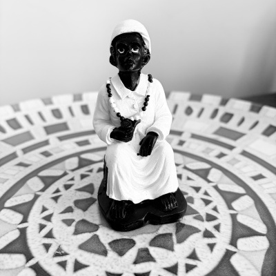 Estátua pequena com figura negra vestindo branco, sobre mesa com padrão geométrico.