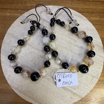 Pulseiras de contas pretas, Âmbar e transparentes com pequenas contas douradas sobre base de madeira clara