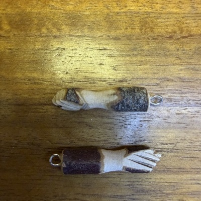 Dois amuletos em madeira com argola metálica sobre madeira clara
