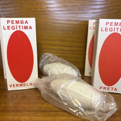 Caixas brancas com oval vermelho e texto PEMBA LEGÍTIMA e objetos brancos embalados em plástico sobre madeira.