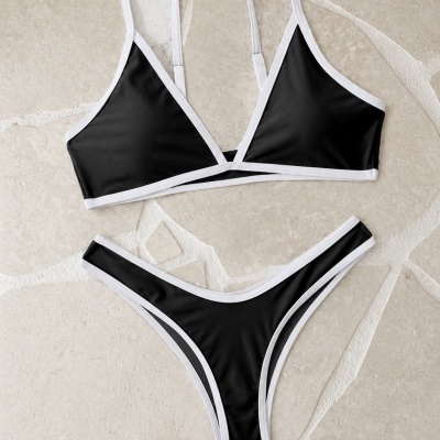 Bikini preto com acabamento branco colocado sobre chão de pedra clara