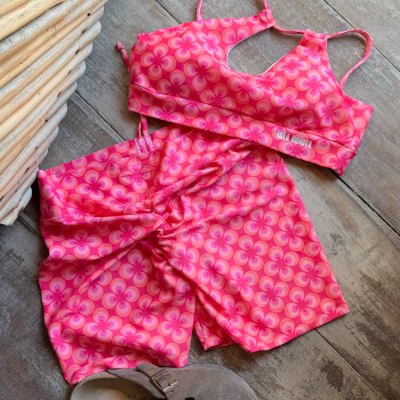 Conjunto desportivo rosa com padrão geométrico, sandálias cinza e pavimento de madeira