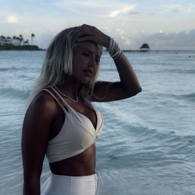 Mulher vestindo roupa branca junto ao mar numa praia com céu nublado