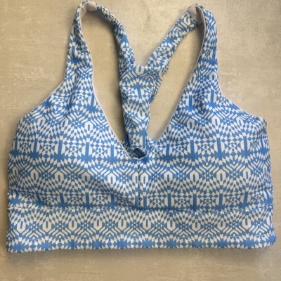 Top desportivo azul e branco com padrão geométrico e alças cruzadas.