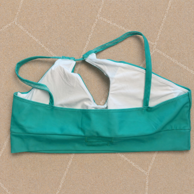 Top de bikini verde água com alças finas sobre chão de azulejos bege