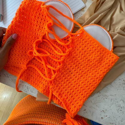 Top de crochet laranja com forro branco sobre mesa branca com caderno aberto e tecido bege