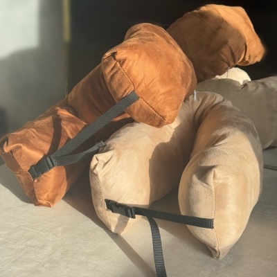 Três almofadas alongadas castanhas e bege com alças pretas sobre superfície clara