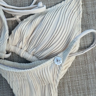 Biquíni branco texturizado com tiras e detalhe LB sobre tecido cinza