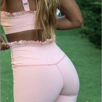 Conjunto roupa fitness rosa claro com top e leggings ajustáveis em ambiente exterior com relvado.