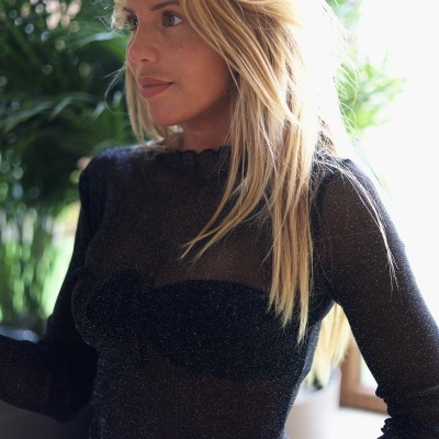 Pessoa com blusa preta transparente brilhante e cabelo loiro junto a janela