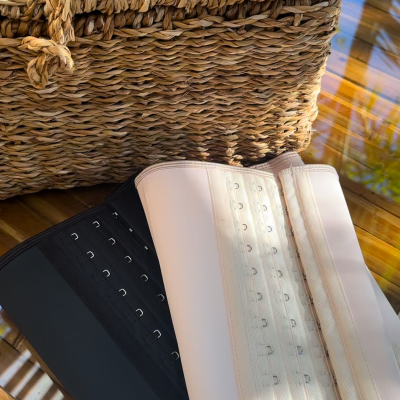 Cintas modeladoras preta e bege com fechos em mesa de vidro e mala de palha trançada