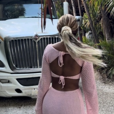 Mulher de costas com roupa rosa em malha rendada e caminhão branco ao fundo