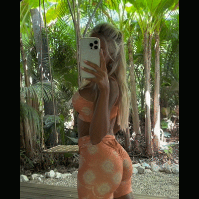 Mulher com conjunto desportivo laranja numa selfie em ambiente tropical