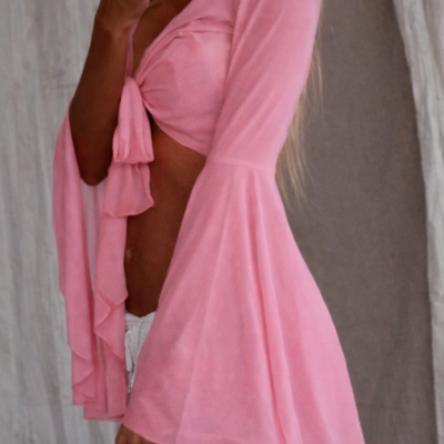 Mulher a usar top rosa com laço frontal e mangas compridas, a tirar selfie com telemóvel branco em fundo neutro