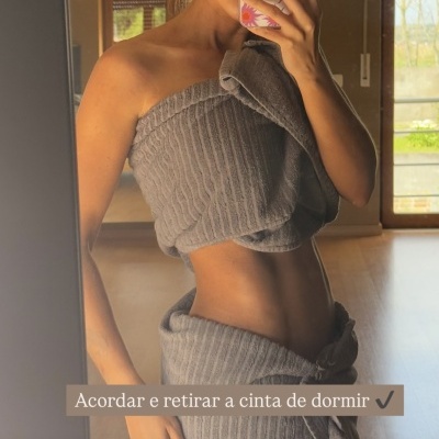 Pessoa a tirar autorretrato no espelho com conjunto cinzento de malha canelada e telemóvel com capa florida.