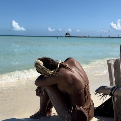 Mulher com biquíni castanho sentada na areia na praia junto ao mar e céu azul