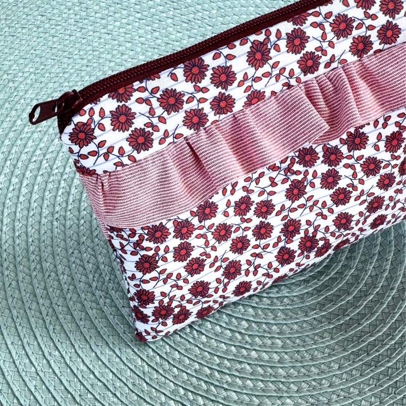 Bolsa de tecido floral vermelha e branca com fecho vermelho e faixa rosa sobre superfície texturada verde