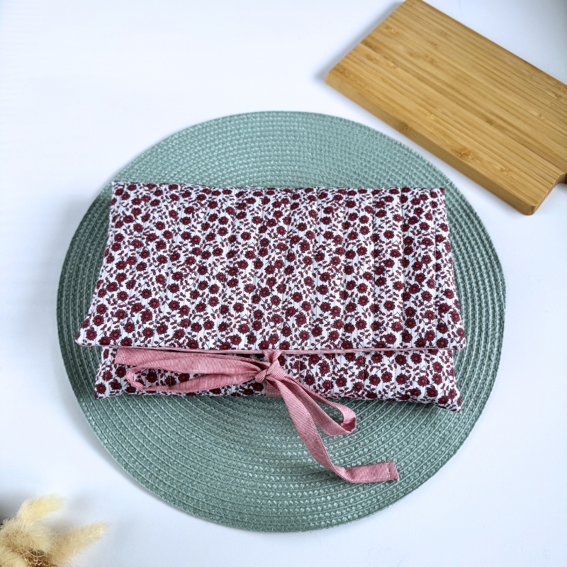 Estojo de tecido floral branco com flores vermelhas e laço rosa sobre prato verde claro