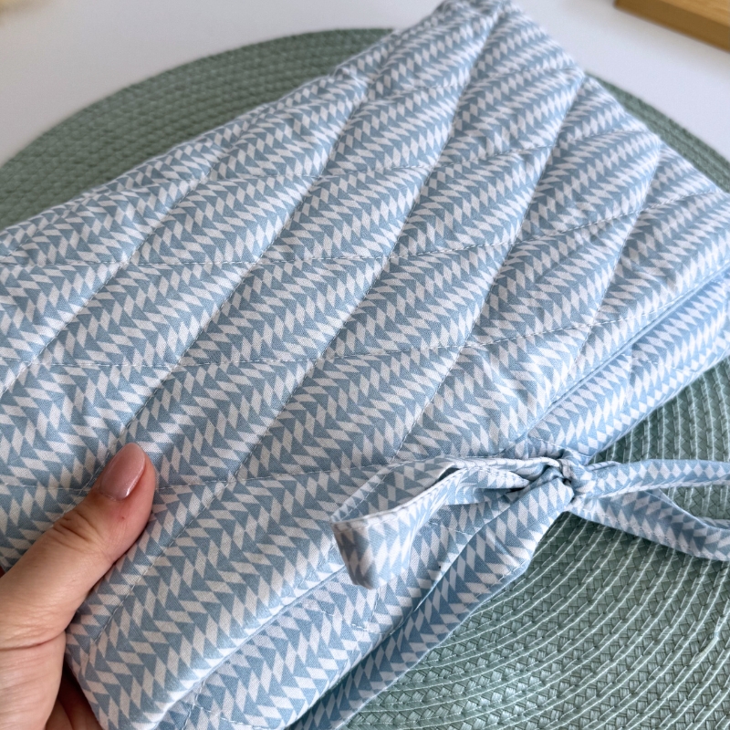 Almofada acolchoada azul claro com padrão de triângulos brancos e laço segurada por uma mão