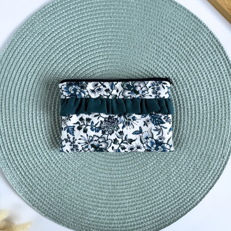 Necessaire floral azul e branca com folho verde sobre tapete verde claro redondo