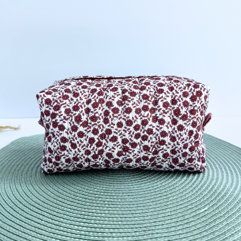 Mala de tecido floral vermelha e branca sobre tapete verde