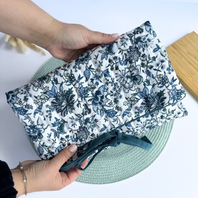 Mala de tecido acolchoada com padrão floral azul e verde, segurada por mãos femininas.